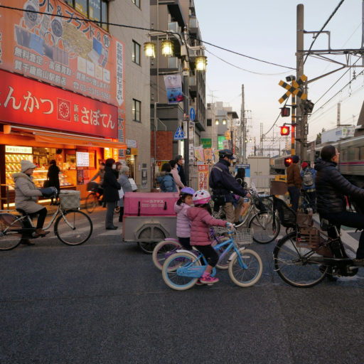 自転車で踏切待ちをしている老若男女の写真