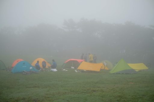 いくつものシェルターと自転車が並ぶ朝のキャンプ場の写真