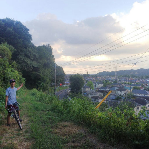 見晴らしのよい丘の中腹の未舗装路で自転車に跨りポーズをとっている人の写真