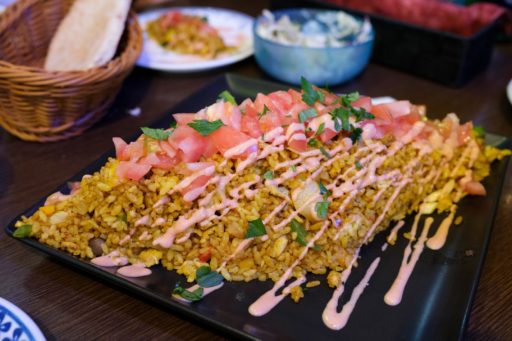 黒い正方形の大皿に盛られたマンサフ。カレーピラフのような見た目。みじん切りにしたトマトとピンク色のソースが掛かっている。