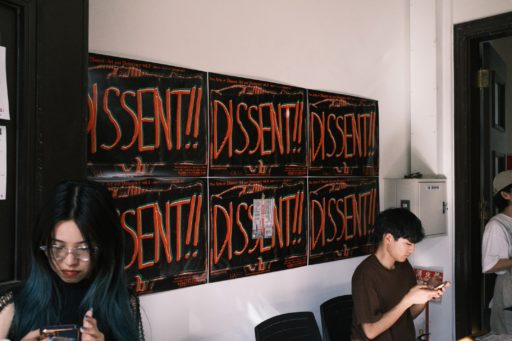 陳列館のエントランスブース。壁に、黒背景に赤い文字で「DISSENT!!」とドローイングされた横長のポスターが6枚貼られている。