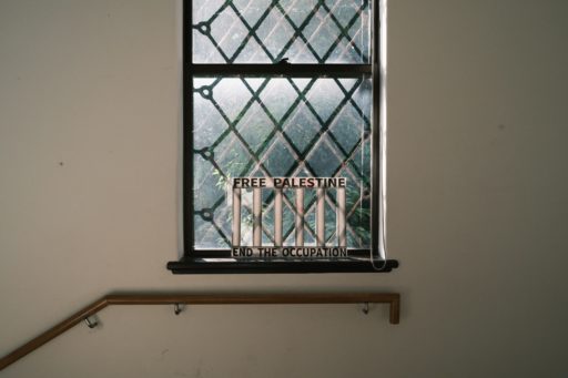 「FREE PALESTINE」「END THE OCCUPATION」と書かれた檻を模したオブジェが、階段の手摺の上にあるひし形の格子が付いた窓の前に置かれている。