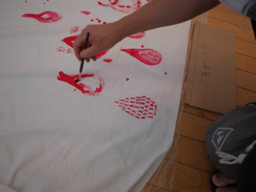 白い布の上に、筆と赤い絵の具で涙を描いている様子。