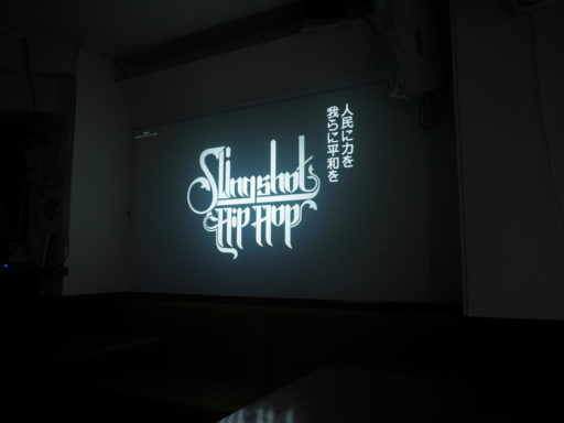 映画の一場面。タイトルロゴの横に「人民に力を　我らに平和を」という字幕。